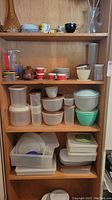 Full view of wooden shelves with multiple plastic food storage containers, cups, bowls, and dishes.