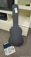 Closed black hard guitar case standing upright with songbooks on floor