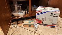 Black and Decker food processor on left, Moulinex meat grinder boxed on right, white mechanical cheese grater and attachments in front on countertop