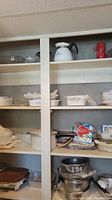 Shelves filled with various kitchenware including CorningWare dishes, glass baking dishes, enamel pots, and more.