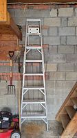 Full view of the aluminum step ladder showing six steps and A-frame design hanging against a cinder block wall in a garage-like setting.