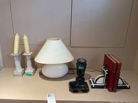 Wide angle showing all items in the lot on a shelf including lamp, candle holders, ashtray, urn, bookends with books