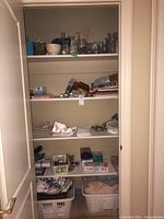 Photo of linen closet shelves showing laundry baskets filled with linens, assorted folded linens, toiletries, and glassware items on shelves