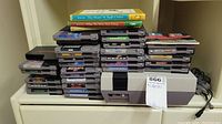 Wide shot of NES console in front of two stacks of game cartridges and controllers and cables at right