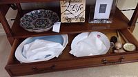 Top view of wooden cabinet drawer showing two platters: a large floral platter and two smaller platters with floral designs, along with small decorative items.