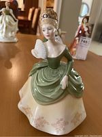 Full view of Royal Doulton porcelain figurine showing seated woman in green evening dress holding fan