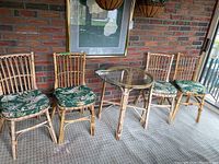 Photo showing full dining set with four bamboo chairs featuring green leaf patterned cushions and round bamboo base glass top table
