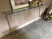 Full front view of clear plexiglass console table with items on the glass top and light carpet background.