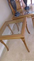 Pair of glass top end tables shown from an angled top view, clear glass is visible with gold-tone frames and curved legs.