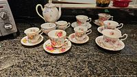 Image showing ceramic teapot, multiple vintage floral teacups and saucers arranged on countertop