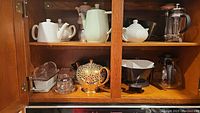Shelf with various teapots, coffee makers, and butter dishes including Sadler teapot and French press