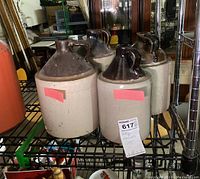 Four antique stoneware jugs on a metal shelf, with two-tone glaze—cream base and brown top and handle