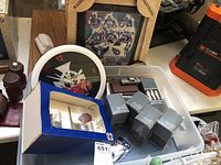 Photo showing the Boondock Saints wall clock with black and white graphic and surrounding red number markings, several boxed pewter cars, a framed sports photo, and key chain in plastic bin