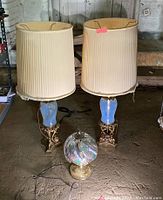 Two tall vintage lamps with blue opaque glass centers and brass-like ornate bases with damaged cream pleated shades. Smaller touch lamp with brass base and multicolored stained glass globe shade in front.