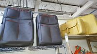 Two Nautica brand soft-sided rolling suitcases in dark grey with orange accents and two vintage yellow vinyl suitcases on a shelf indoors.