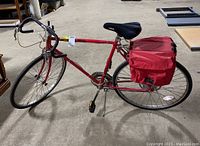 Red men's 10-speed road bike with drop handlebars and attached rear red travel totes, side view showing full bike profile.