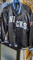 Full view of Puma satin black jacket with 'NICKS' lettering on front and striped cuff, collar, waistband.