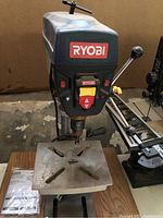 Front view of Ryobi drill press showing the control panel with various colored switches and the brand name.