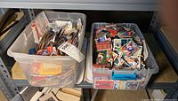 Two plastic bins filled with assorted sports cards positioned on a shelving unit.