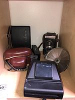 Full lot view showing Polaroid Land camera, Berkley XR106, Graceflex TLR medium format camera, Voigtlander Vito CL, Kodak instant camera with leather case, and Accura reflector inside a wooden cubby