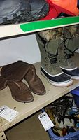 Two pairs of boots on a shelf, showing the full Sorel winter boot with fur trim and brown leather cowboy boots side by side.
