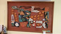 Full view of the mosaic wall art on wood showing abstract underwater scene with fish shapes and varied ceramic tile pieces in earth tones.