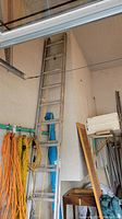 Photo of a 12 foot aluminum extension ladder leaning against a garage wall with extension rope visible and various garage items around.