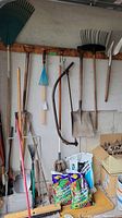 Wide view of garden tools hanging on wall and standing against the wall plus bags of soil on the floor.