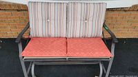 Front view of metal glider bench with striped back cushions and red patterned seat cushions.