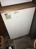 White Indesit mini bar fridge, front view showing the control panel and door surface, placed on stone floor