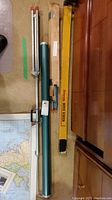 Three vintage projector screens laid flat near wooden cabinet: Yellow Brownie Movie Screen box, green metal tube case, and a cardboard box labeled Tube Screen.