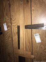 Photo showing three metal squares and two wooden T-squares leaned against a wood-paneled wall.