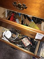Open two wooden drawers showing assorted hand tools including multiple screwdrivers with various handles, a smoke alarm box, wire clippers, drill bits, and metal measuring square.