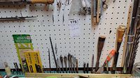 Close-up photo of drill bits including spade bits, screwdriver bits, drill accessories and wooden-handle brushes mounted on pegboard