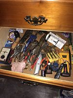 Top view of wooden drawer containing assorted hand tools and electronic testers. Wrenches, pliers and packaged cable stripping tool visible.