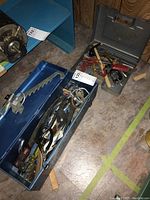 Open blue metal tool box showing a metal hand saw, several hand tools including pliers and wrenches inside.