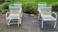 Four vintage metal garden chairs on a patio, two of which are glider chairs, featuring white frames and multicolored slatted seats and backs.