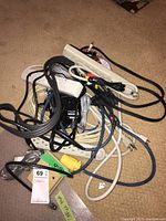 Loose pile of electrical cords and power strips showing various types and colors of cables mixed together on carpet