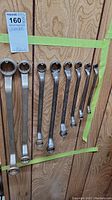 Photo showing set of eight large combination wrenches taped on wooden board, arranged by size largest to smallest.