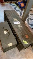 Wide angled photo showing the large WWII mine box and the smaller metal tool box placed on floor tiles.