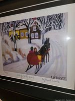 Close-up of the framed fine art print showing the signed title 'Sleigh Ride Home' and artist signature 'Maud Lewis' with a horse-drawn sleigh and winter scene.