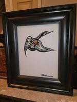 Framed painting showing black bird design with red, yellow, and beige highlights.
