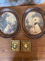 Two large oval framed prints and two small rectangular miniature floral portraits on wooden floor.