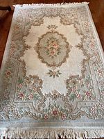 Full view of the hand-hooked Palace area rug showing floral medallion pattern and border design with fringe edges on wooden floor.