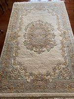 Full view of rectangular area rug with central medallion and floral border in muted pastel colors.