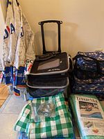 Photo showing outdoor entertaining items including folded Molson Canadian branded patio umbrellas, stacked Glacier Pack and Backsaver cooler bags, green and white checkered tablecloth, and leisure mats.
