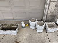 Wide view showing all seven items: two large urns, two rectangular planters, one large white duck statue and two smaller yellow duck statues.