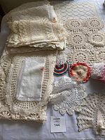 Overview of multiple folded crochet linens and doilies laid out on a table including table runners and smaller cloth pieces with various crochet lace patterns.