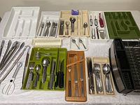 Photo of various utensil trays with cutlery including forks, spoons, knives, tongs, and kitchen tools spread on a table