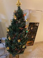 Photo of fully assembled fiber optic Christmas tree with gold lantern decorations and star topper, plugged in and lit with multi-colored fiber optic lights.